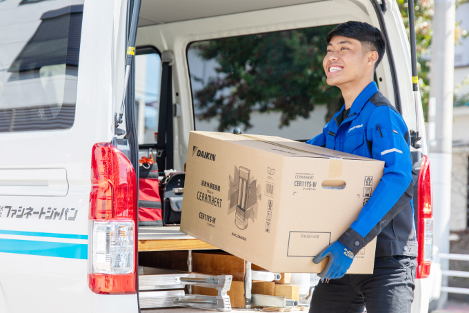 「ファシネートジャパン」の青い制服を着た男性が、社名入りの車両からダイキン製機器(セラムヒート)の梱包箱を運び出している様子