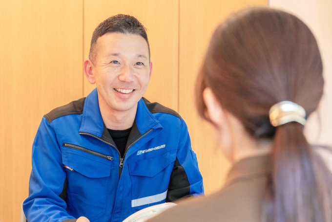 「ファシネートジャパン」の青い制服を着た男性が、対面の人物と笑顔で会話をしている様子