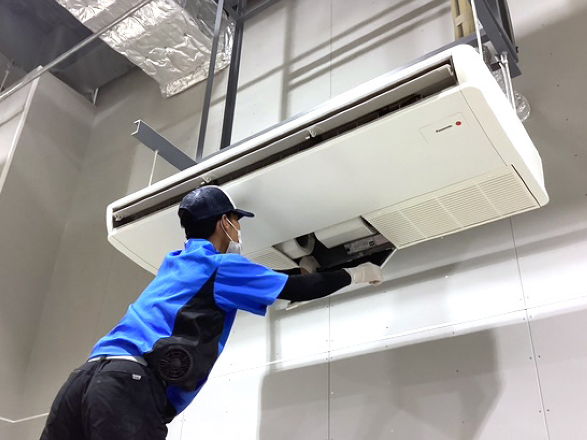 男性が天井吊り下げ型空調機器のメンテナンス（点検や清掃など）を行っている様子
